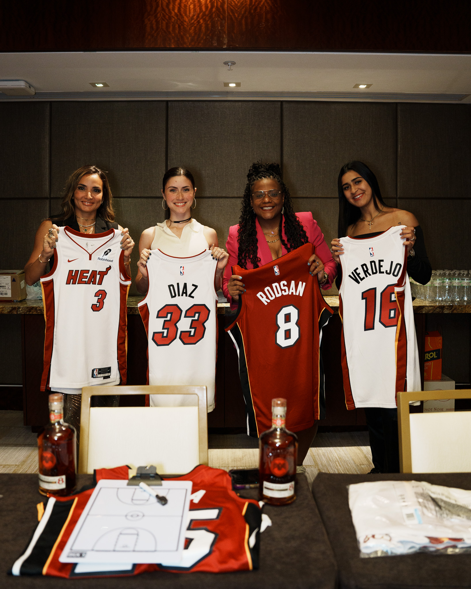 Celebrity Game participants holding personalized Miami Heat jerseys backstage